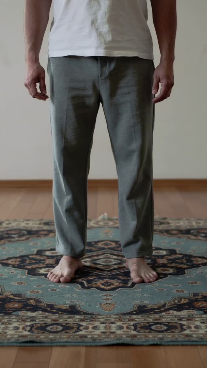 Video verticale: Uomo in maglietta bianca e pantaloni grigi che fa piccoli spostamenti con i piedi per mantenere l'equilibrio su un tappeto ornato