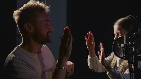 a young girl records a song in a recording studio, being encouraged by a man