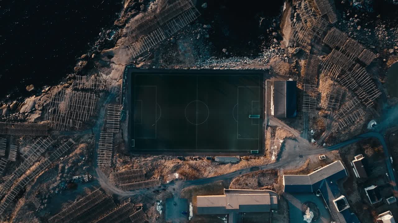 Top View Of Soccer Field At Reine Stadion Surrounded By Rugged Terrain And Coastal Waters In Reine, Norway. aerial shot