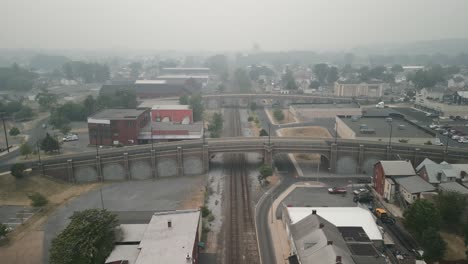 Vista-Aérea-De-Drones-De-Vehículos-Que-Pasan-Por-El-Puente-Del-Ferrocarril-En-Una-Espesa-Neblina-Y-Smog