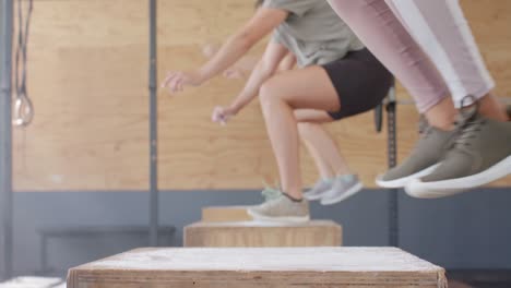 unaltered diverse women jumping on boxes and training at fitness class in gym, slow motion