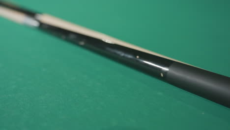 close-up shot of cue stick laid on green pool table, with colorful billiard balls neatly arranged in triangle rack, ready for a game in a cozy, relaxed atmosphere