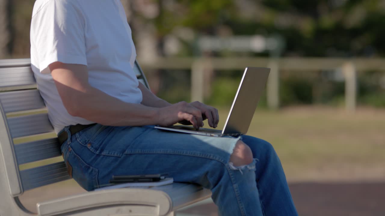 Closeup Man Typing on Laptop sitting on metal park bench outdoors