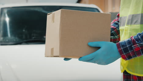 Un-Mensajero-En-Uniforme-Sostiene-Un-Paquete-Con-El-Telón-De-Fondo-De-Una-Camioneta-Blanca