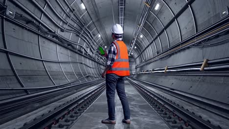 full body back view of asian male engineer with safety helmet working on a green screen smartphone and looking around while standing in underground subway tunnel