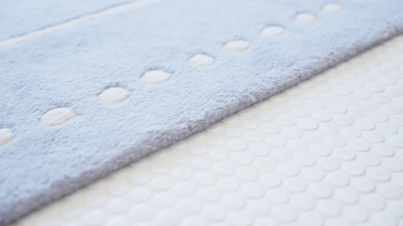 Close-up of a soft blue bath mat on a white penny tile floor, showcasing clean textures and a calm, minimalist design in a bright modern space