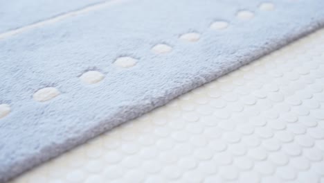 close-up of a soft blue bath mat on a white penny tile floor, showcasing clean textures and a calm, minimalist design in a bright modern space