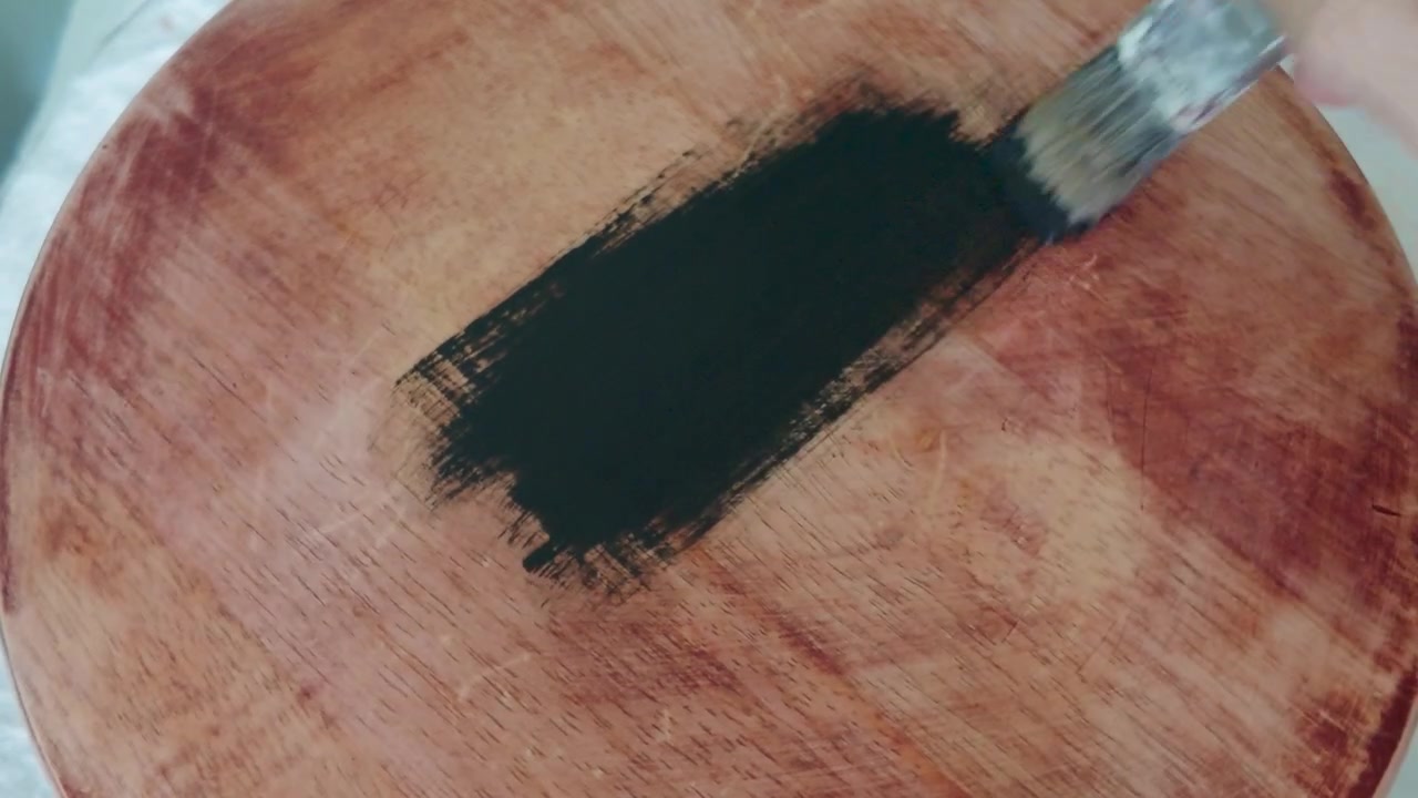 Dipingere un tavolo levigato con vernice nera mentre un pennello ricopre la superficie di legno grezzo in un progetto fai-da-te di riciclo creativo di mobili e miglioramento domestico, vista ravvicinata dell'artigianato e del lavoro di ristrutturazione