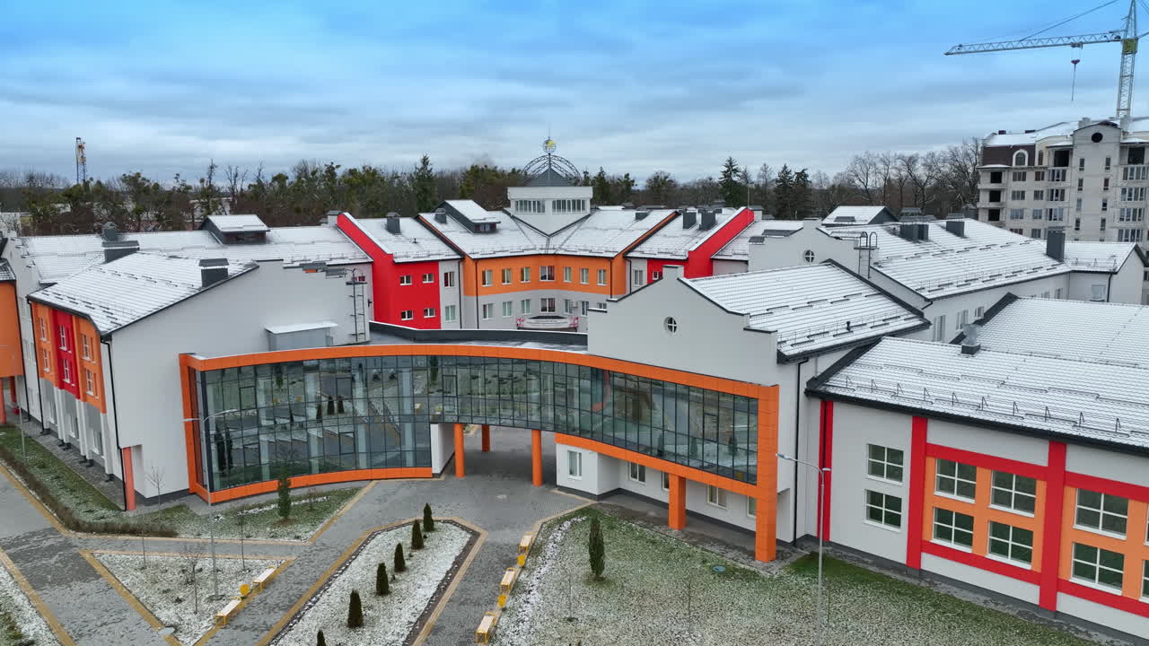 Modern design of the building with the unusual shape. Bright colored walls and mirrored windows in the building. Lawn with young trees at the forefront.
