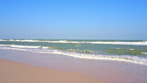 beautiful clean white foamy sea waves crashing against an empty yellow sand beach at the daytime blue cloudless sky