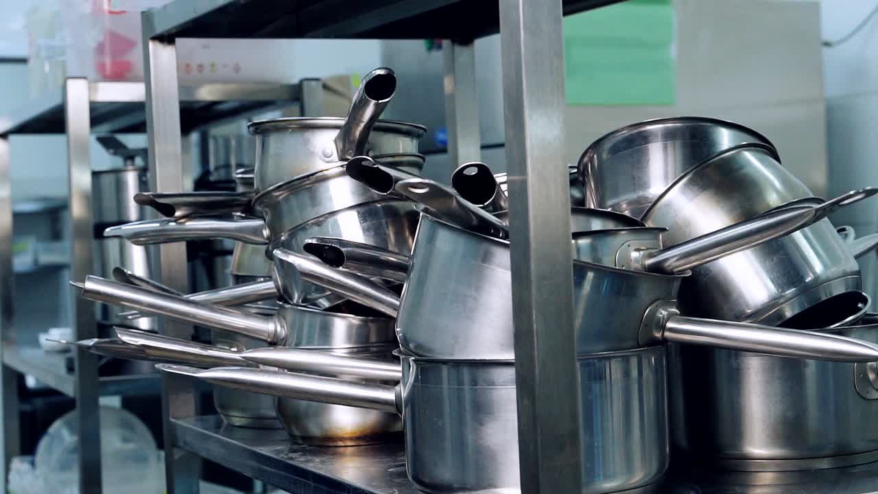 Clean cooking equipment in kitchen restaurant. Sets of cooking bowls and pots. Metal kitchen utensils on stand. Kitchenware