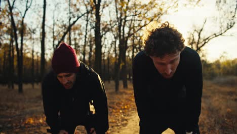 A-guy-in-a-red-cap-a-brunette-with-a-beard-in-a-black-sports-uniform-together-with-his-friend-a-man-with-curly-hair-are-running-to-their-destination-after-their-jogging-in-the-autumn-park-at-Sunrise-in-the-fall