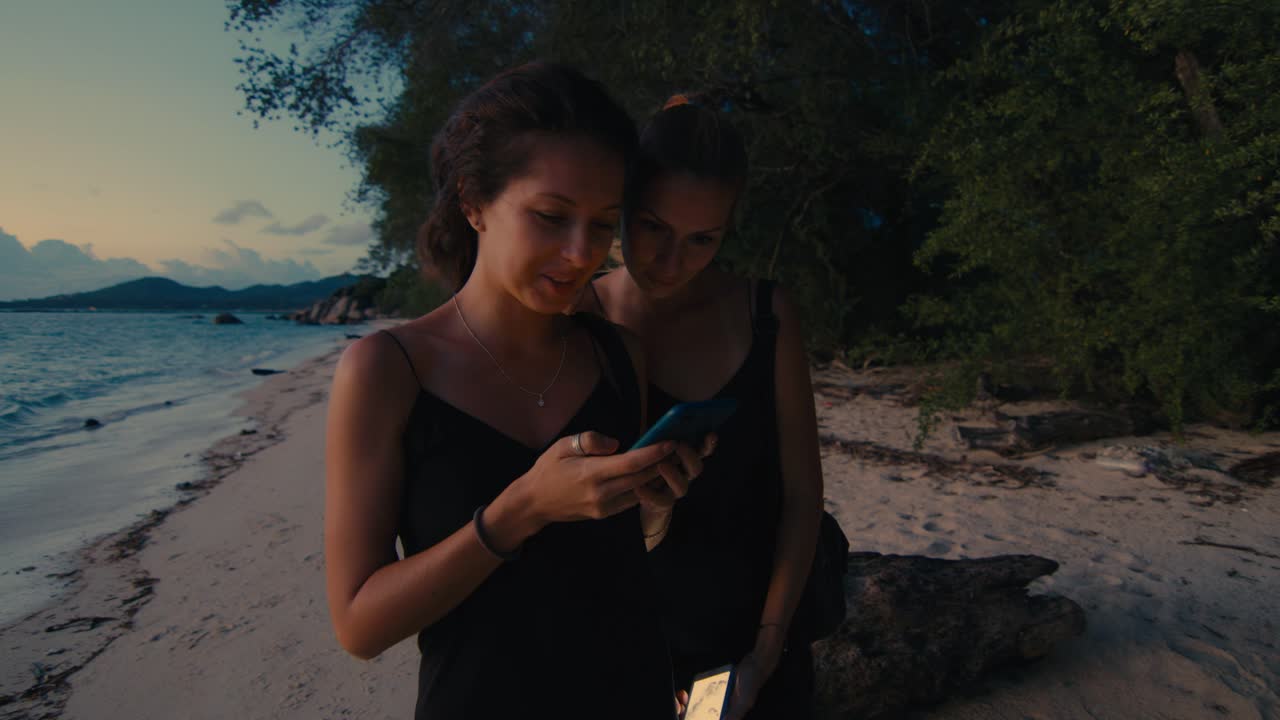 Two friends on a beach at sunset using their phones