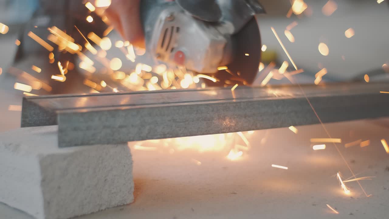 남자는 원형 도자기를 니다. 뜨거운 금속에서 불꽃이 날아갑니다. 남자는 강철 위에서 열심히 일합니다. 차고에서 찍은 클로즈업 느린 동작입니다.