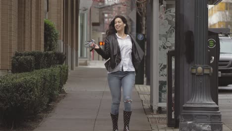 young beautiful latin woman dancing around with an umbrella in the city while listening to music. she then splashes around on a puddle