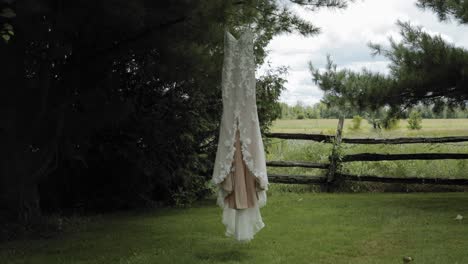 elegante vestido de boda blanco de diseño que cuelga del pino en el patio trasero de una superficie con árboles, una valla de madera y un campo de cultivo al fondo en el centro de eventos y bodas de strathmere