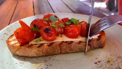 cutting a delicious bruschetta sourdough toast with cherry tomatoes and fresh basil, traditional italian breakfast brunch dish at a restaurant, 4k shot