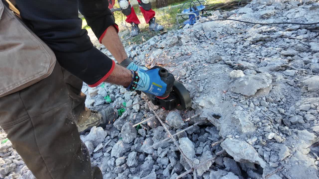 Close up view of man cutting steel fiber-reinforced concrete's construction iron with a round iron cutting machine on a sunny day,sparks over debris.Sun beams on man and debris.