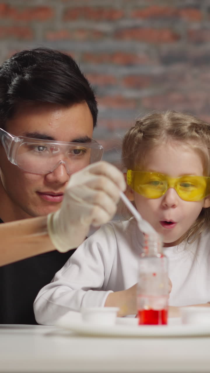 Asian man pours catalyst and little girl student wondered of rising up color drops with African-American teacher in studio slow motion