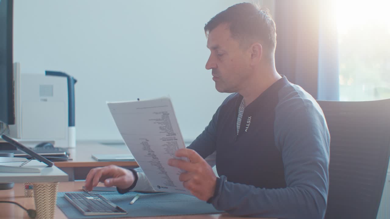 busy European Dutch Caucasian white man male adult model working in the office job on desktop workspace with paper documents and typing on pc keyboard, digital film look
