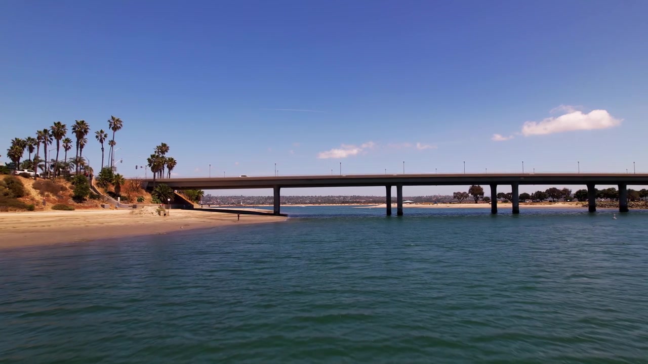 Dron rychle letící dozadu v Mission Bay Parku v San Diegu v Kalifornii s kamerou naklánějící se nahoru, aby odhalila most a zátoku.