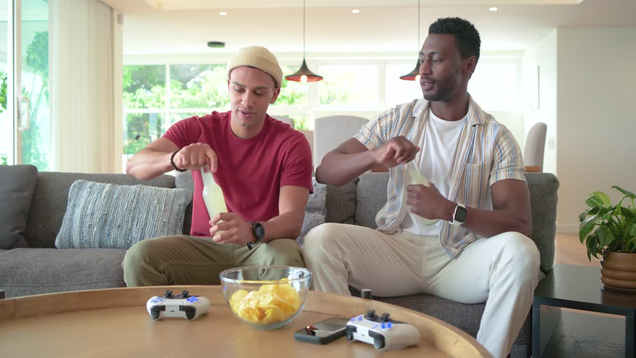 Diverse male friends at home bringing bottles opening near controllers and sipping before gaming