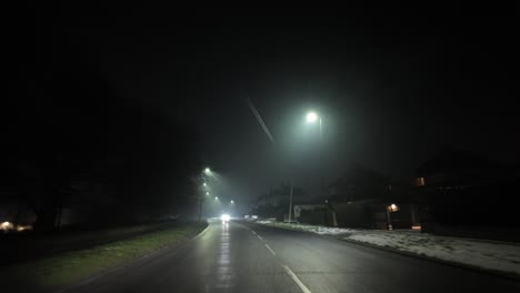 dimly lit foggy road at night with glowing streetlights and snow along the sides.