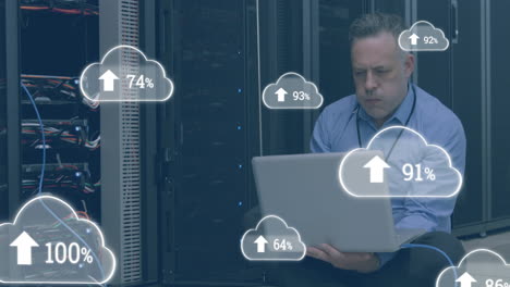 animación de nubes con números sobre hombre caucásico estresado trabajando en una computadora portátil en la sala de servidores