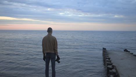 Rückansicht-Eines-Jungen-Fotografen,-Der-Am-Ufer-Steht-Und-Den-Wunderschönen-Blick-Auf-Den-Sonnenuntergang-Genießt---Weitschuss