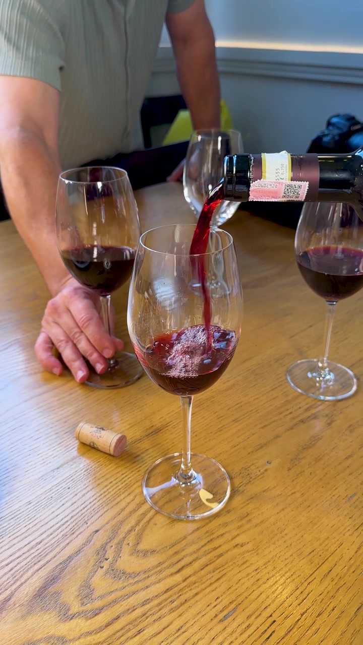 Primo piano di vino rosso che viene versato in un bicchiere di cristallo su un tavolo di legno.