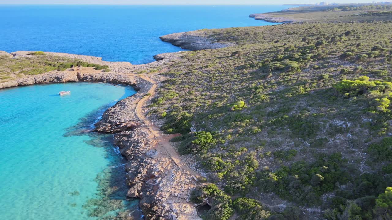 Experience breathtaking aerial views of Mallorca's coastline showcasing the beautiful Cala Varques area. Lush greenery complements the stunning blue waters under clear skies.
