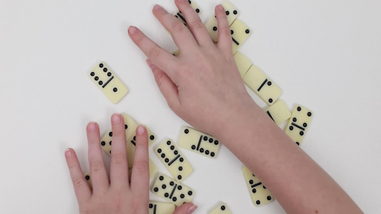 Dominoes being played with hands on a white table