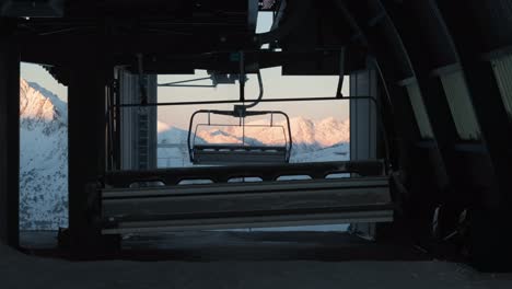chairlifts arrive and turn at the top station, shaded, with sunlit snowy mountains in the background in andorra.