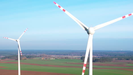 Close-up-drone-shot-of-rotating-white-windmills-on-rural-area-during-blue-sky-in-nature