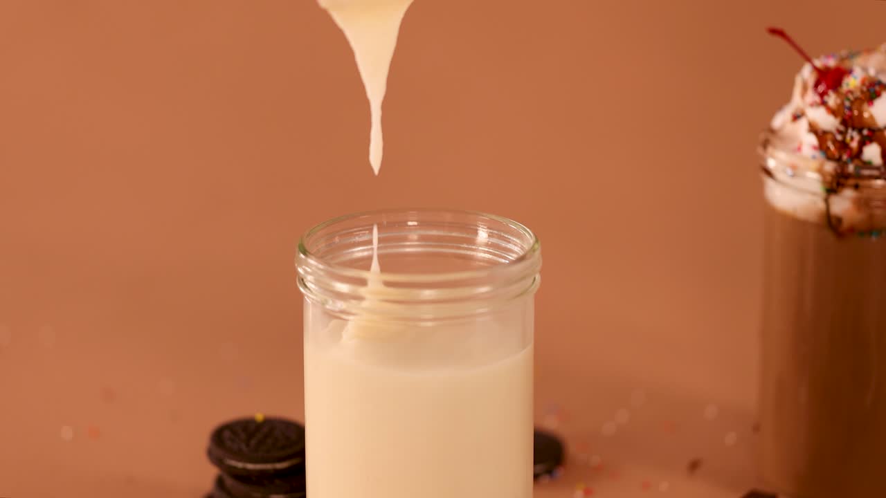 Frappè alla vaniglia versato in un barattolo di vetro, circondato da biscotti, cioccolato, illuminazione calda da studio, scatto statico