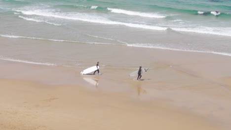 two surfers carrying their surfboards by the beach at praia do guincho, portugal