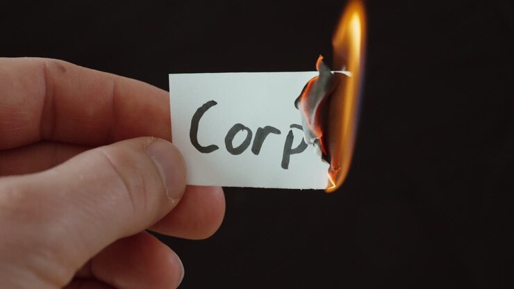 Hand burning a paper labeled “Corporate,” symbolizing business crisis, loss of values, and ethical issues in companies