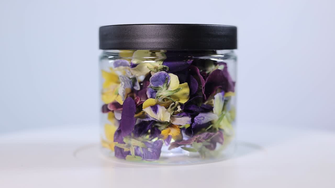 A clear jar containing vibrant yellow and purple freeze-dried Viola wittrockiana petals. Perfect for culinary decoration, teas, or crafts.