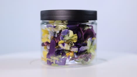 a clear jar containing vibrant yellow and purple freeze-dried viola wittrockiana petals. perfect for culinary decoration, teas, or crafts.