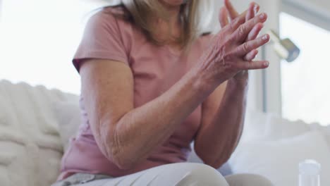 Mid-section-of-senior-woman-sanitizing-her-hands-at-home