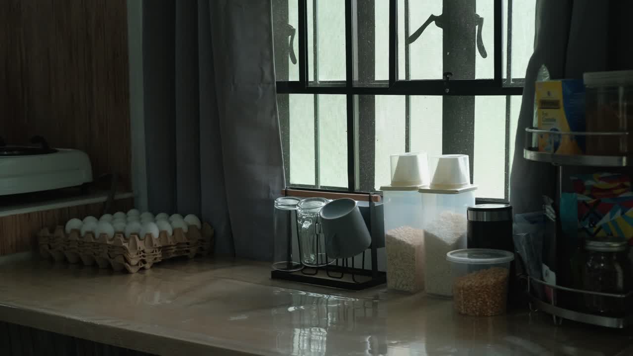Eggtray and toaster being placed on a cozy kitchen table by sunlit apartment window. -static wide shot