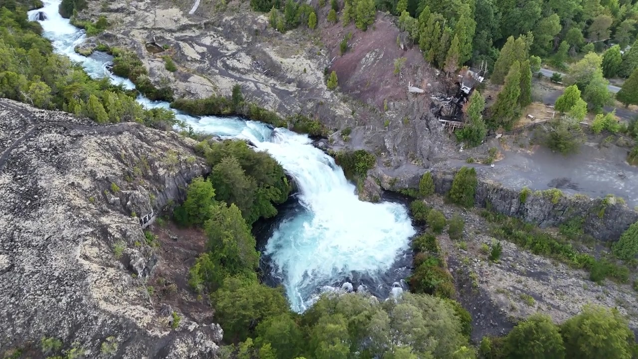 Aerial drone footage pushing forward over the Truful Truful River waterfall in Conguillio National Park. Turquoise whitewater cascades through volcanic lava rock canyon