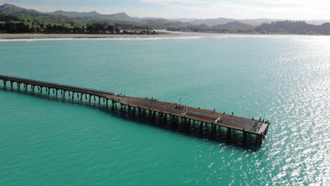 beautiful aerial of tolaga bay, people walking on the longest wharf in new zealand, mountain scenery reveal