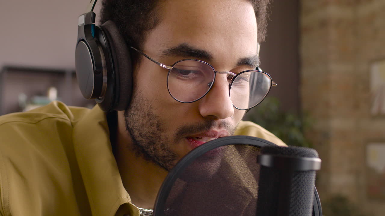 vista de cerca de un hombre con gafas mientras habla por un micrófono y graba un podcast 1