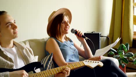 creative musical duet is practising at home woman is singing in microphone and man is playing the guitar. young cheerful people are wearing casual clothes.