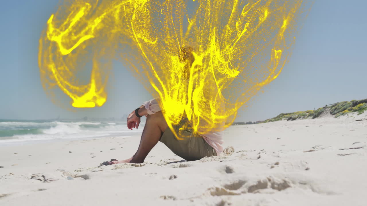 Senior man sitting on sandy beach, showing technology with smartwatch and yellow particles swirling