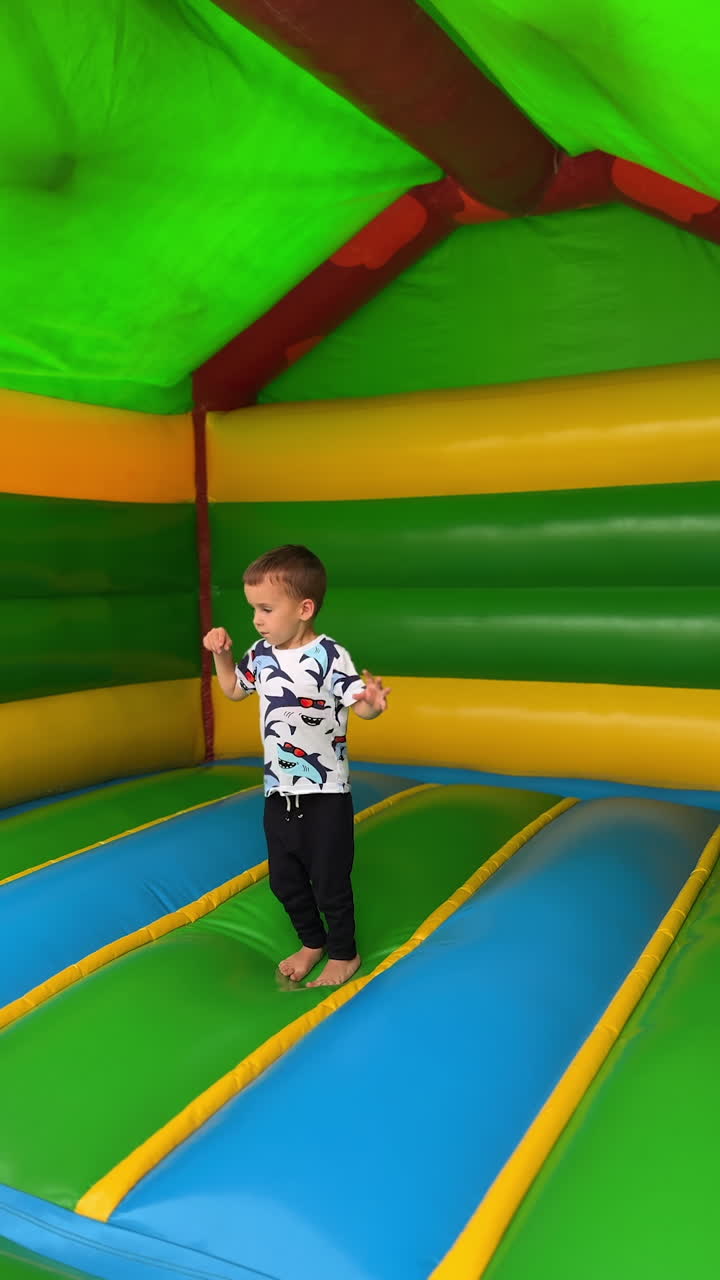 Little baby boy jumping cheerfully inside the inflatable playhouse. Active fun time for a toddler kid. Vertical video.