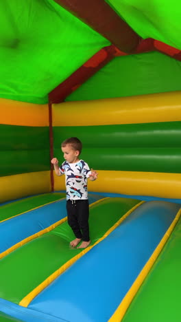 little baby boy jumping cheerfully inside the inflatable playhouse. active fun time for a toddler kid. vertical video.