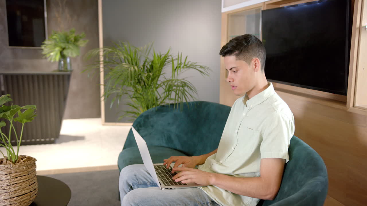 Typing on laptop, young man working remotely in modern office space
