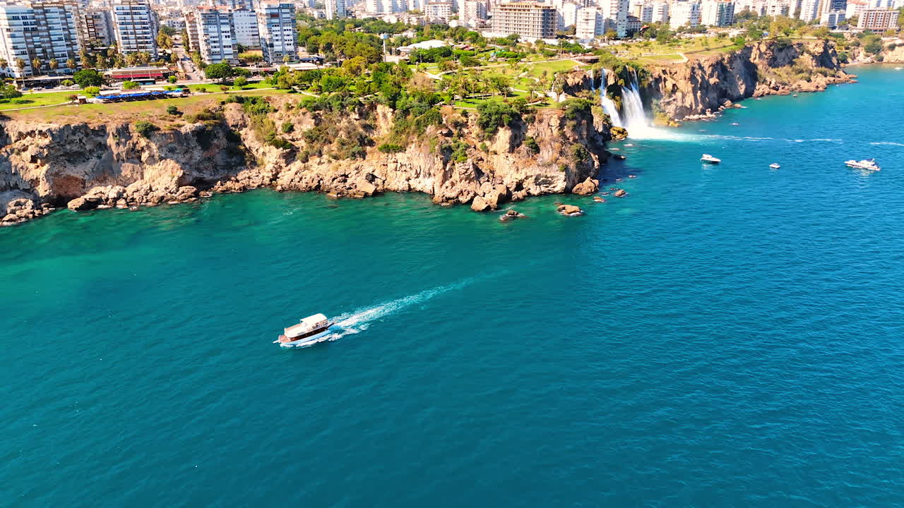 Un motoscafo si muove nelle acque azzurre del Mar Mediterraneo. Vista aerea sulla costa rocciosa con le cascate nella provincia di Antalya, Turchia meridionale.